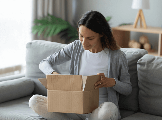Young woman sat on sofa looking in package