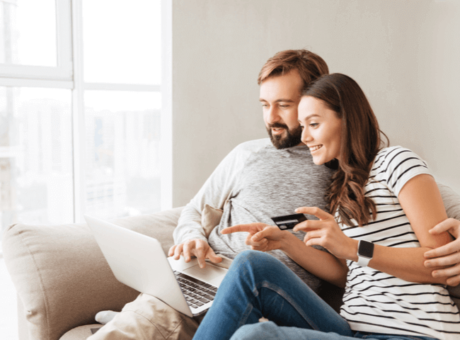 Young couple sat on couch with laptop