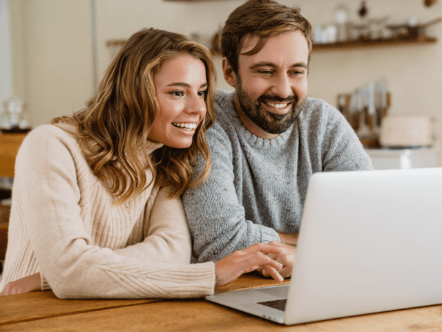 Couple smiling and using laptop while sitting in cozy kitchen
